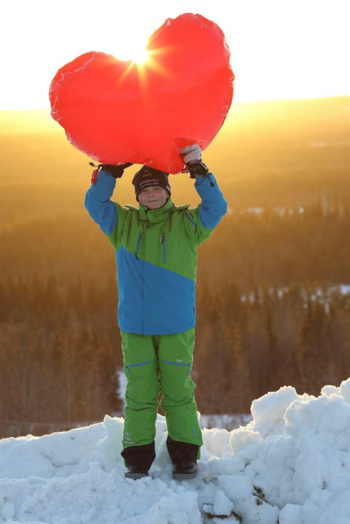Ett barn håller ett stort plasthjärta ovanför huvudet, solen strilar igenom