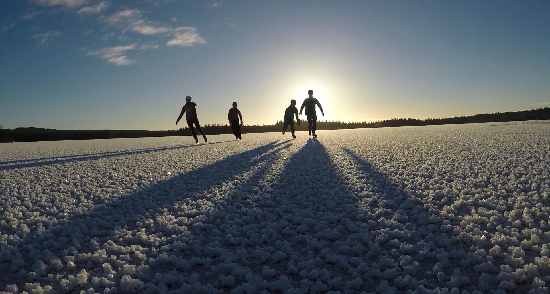 Fyra personer åker skridskor på isen i motljus